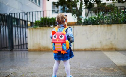 small girl with colourful backpack looks at the entrance to a daycare centre